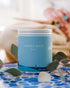 A Large Blue Tin With scenes of water on the side. Made in the USA In Kalamazoo, MI. Scented with Citrus, Herbs, Earth.