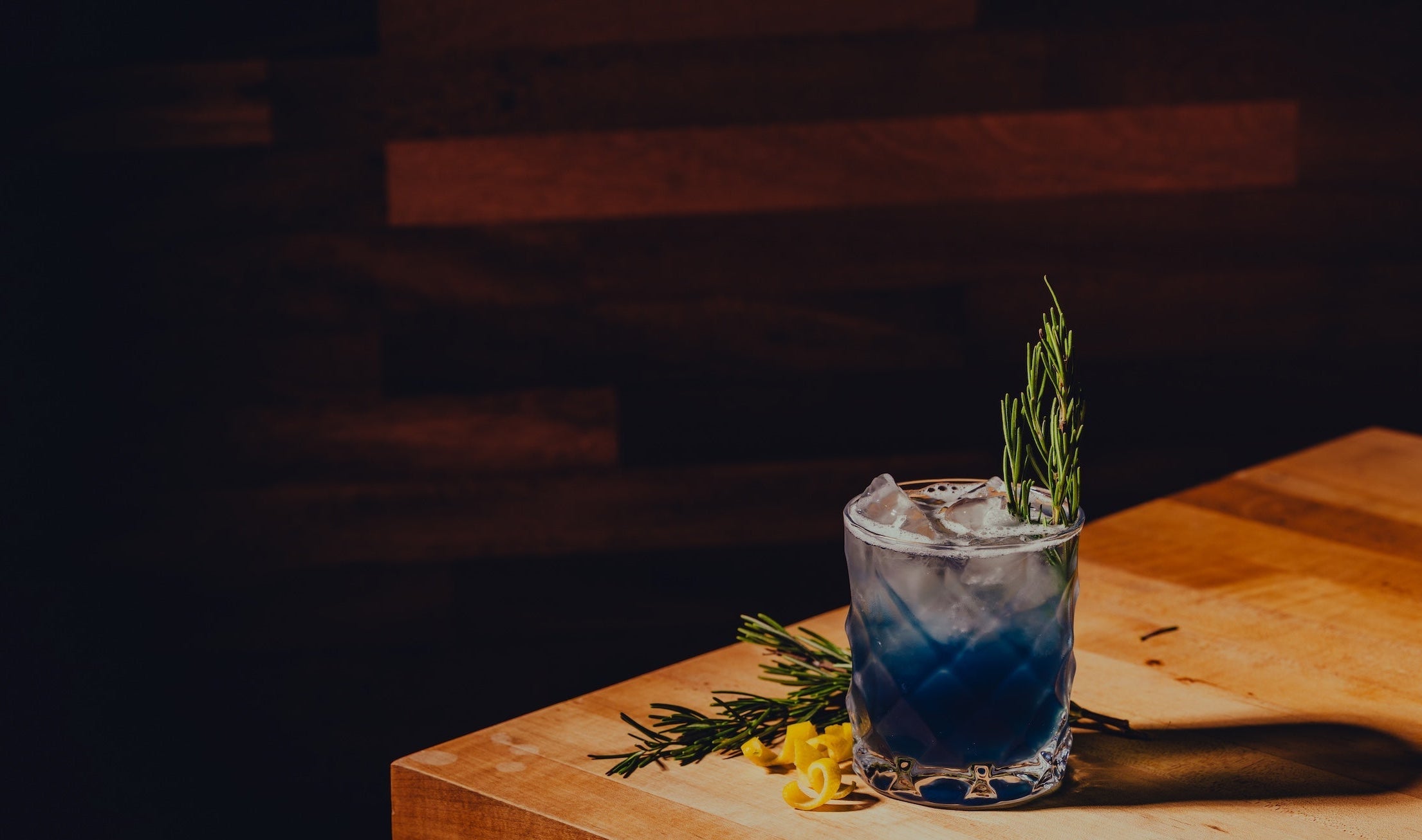 Blue cocktail with a sprig of rosemary on a wooden surface against a dark background