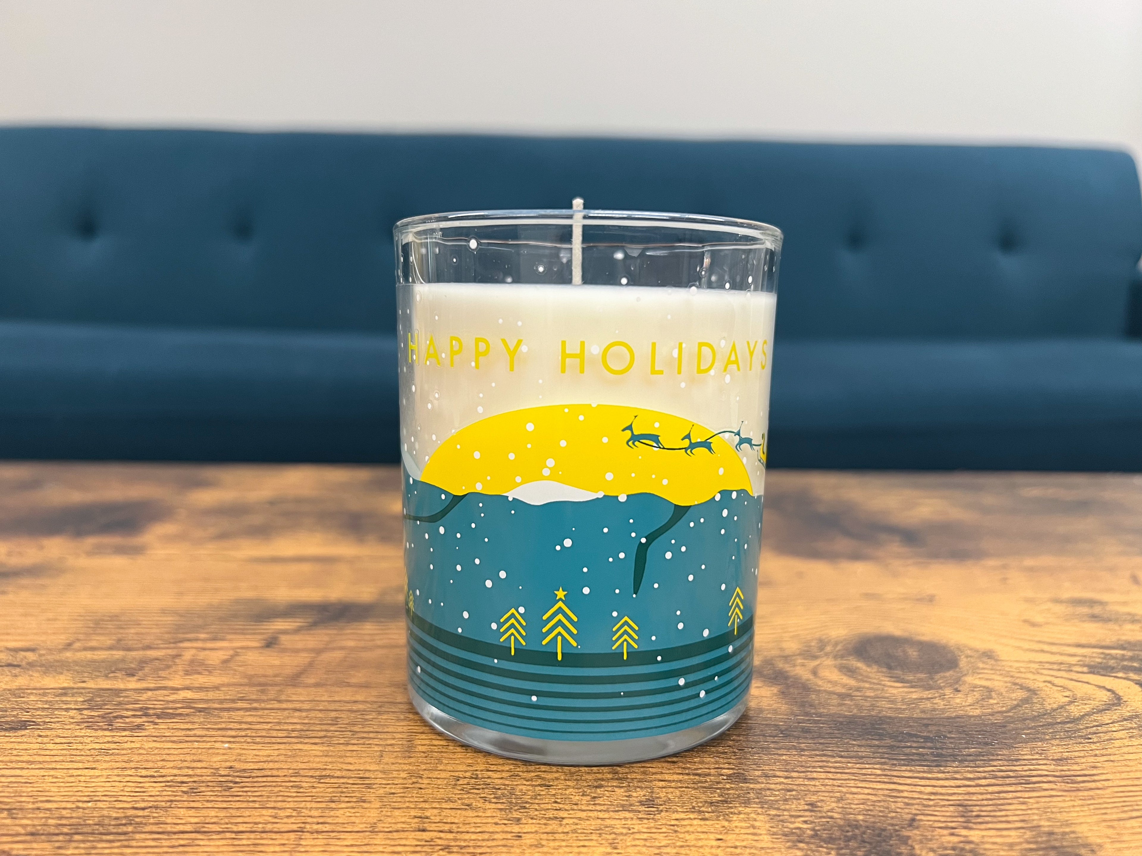 The 2023 Holiday jar sitting on a wooden table in front of a blue couch and a gray wall.