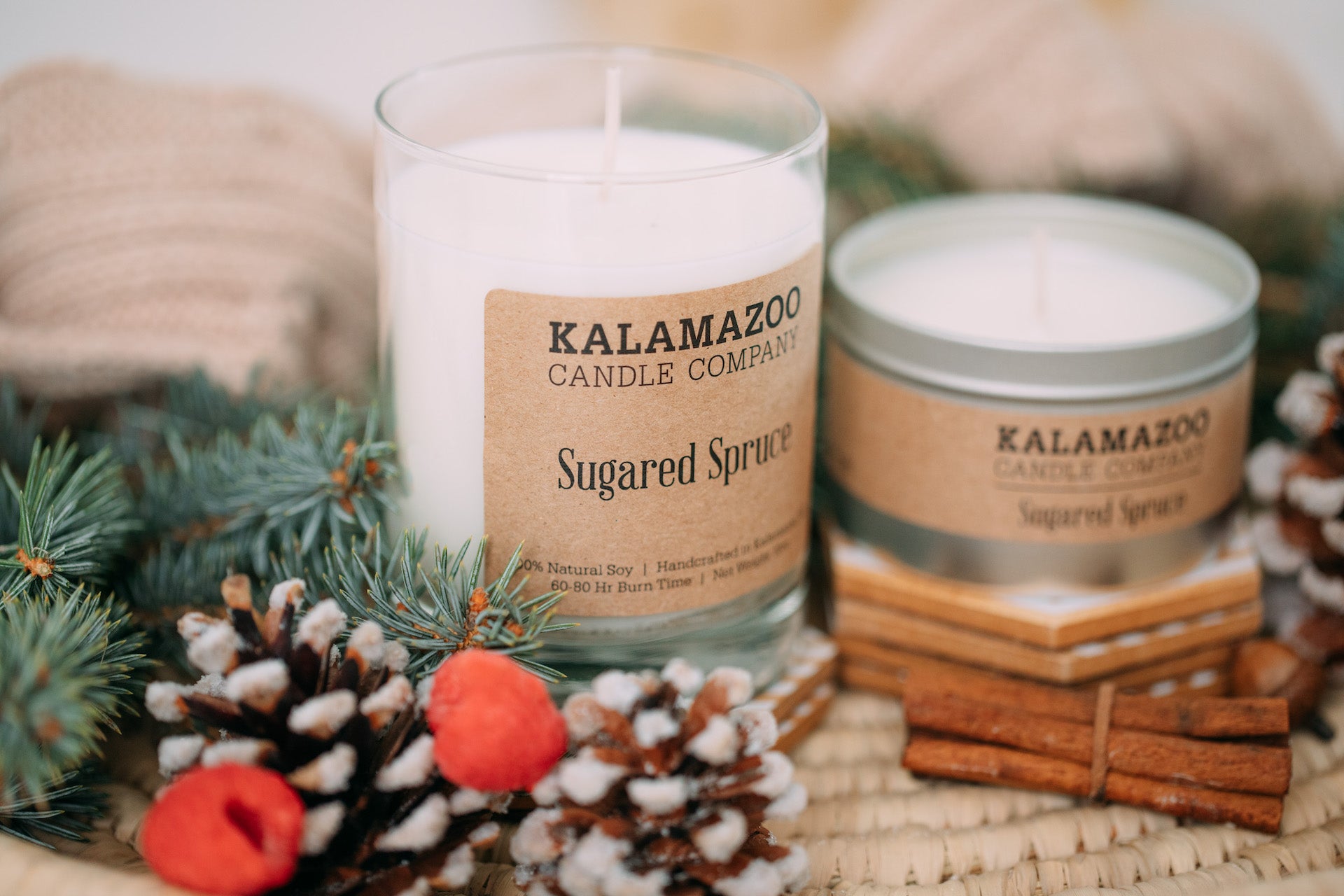 Two Sugared Spruce candles surrounded by winter foliage.