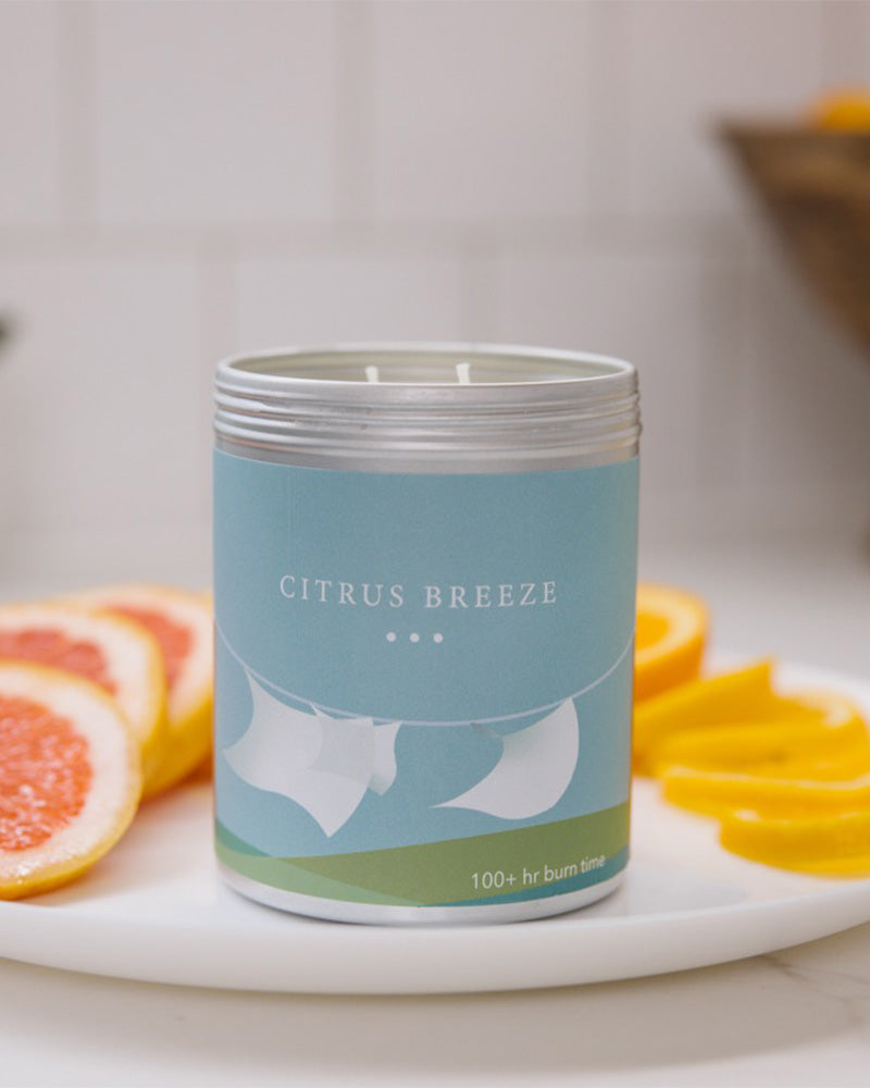 A Large blue candle tin with laundry blowing in the breeze on the side. Made in Kalamazoo, MI USA. Scented with Citrus, Fresh Laundry, and Earth.
