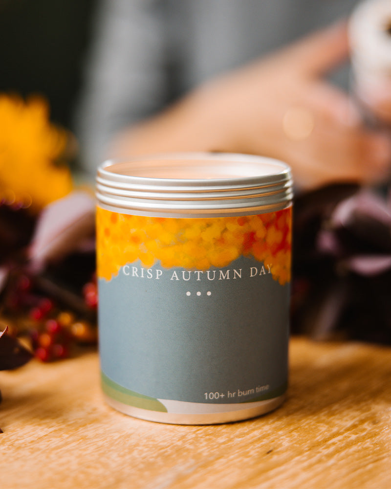 A Large Blue-Grey candle tin with Autumn leaves and trees on the side. Made in Kalamazoo, MI USA. Scented with Blood Orange, Yuzu Zest, and Autumn Breeze.