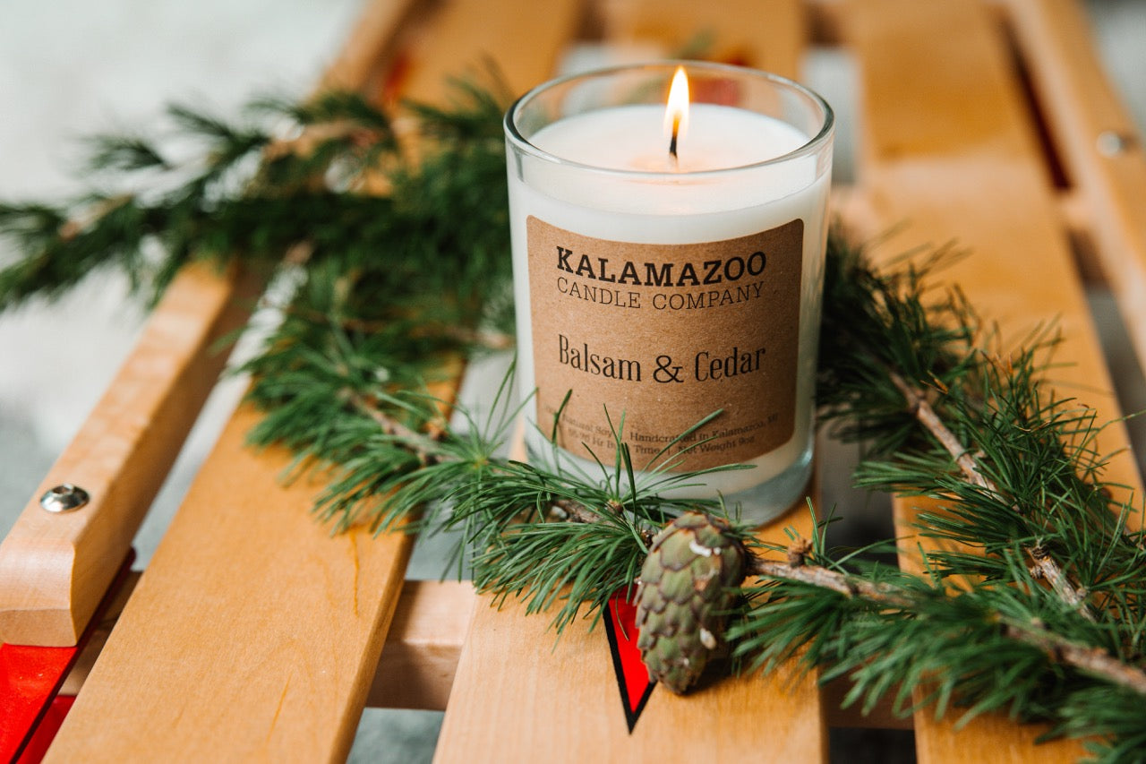 A Balsam & Cedar Candle with a fir tree leave and sled.