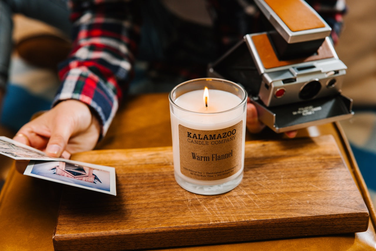 A Warm Flannel Candle on a brown box with polaroids.