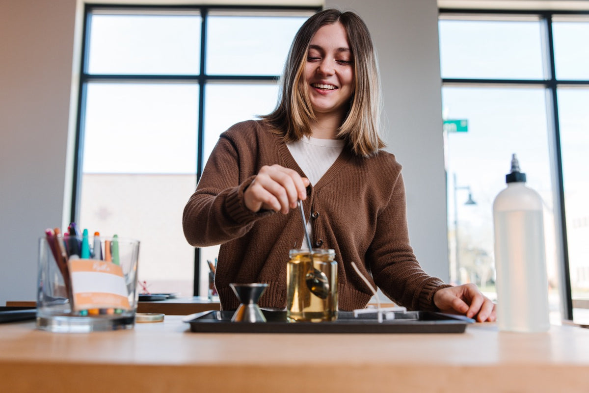 Smiling guest stirring fragrance into her candle at the make-your-own candle bar