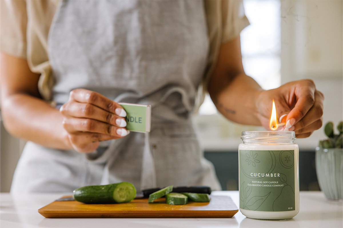 Hand lighting a cucumber candle with a match.