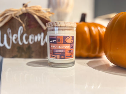 A candle called &quot;Cozy Crafternoon&quot; In front of fall pumpkins