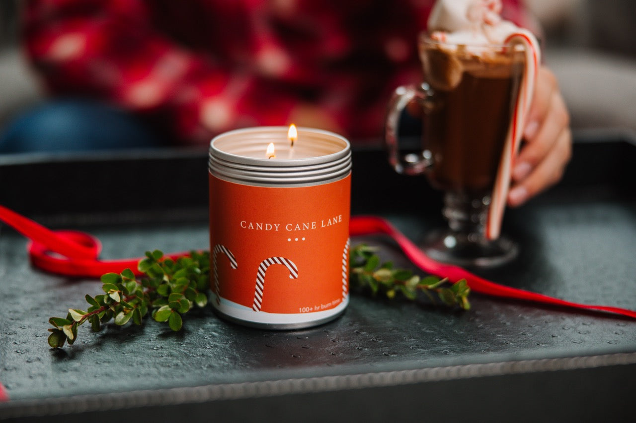 A Candy Cane Lane Candle Burning next to a mug of hot chocolate