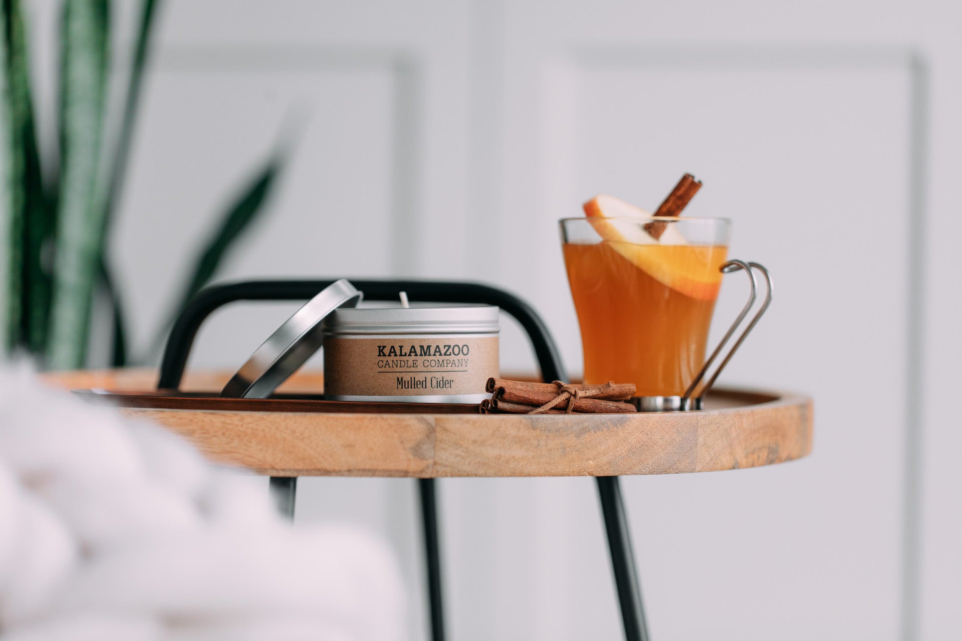 A mulled cider candle tin next to a glass of cider