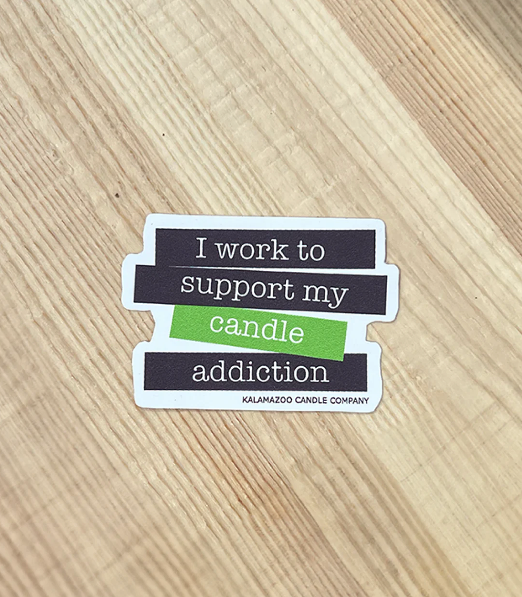 A Black and Green Sticker that says &quot;I work to support my candle addiction&quot;. 
