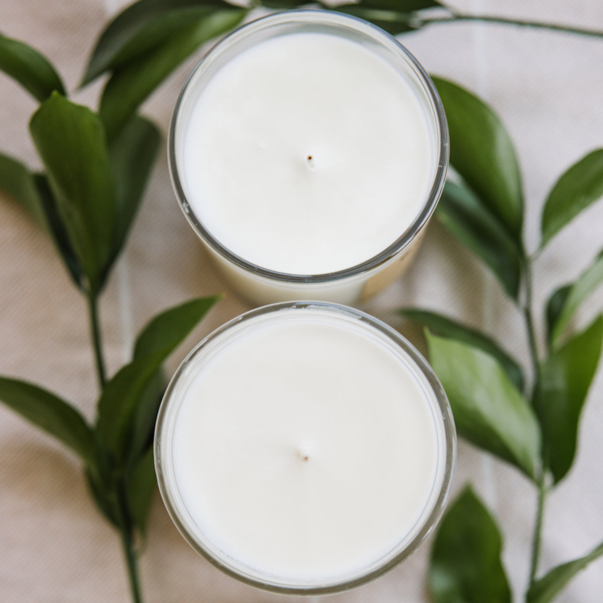 Overhead view of white soy candles in glass jars with green leaves