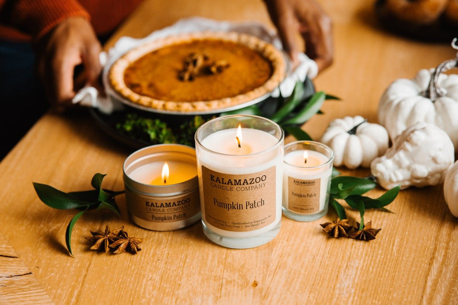 Pumpkin Patch soy candle jar, travel tin and votive lit beside a pumpkin pie