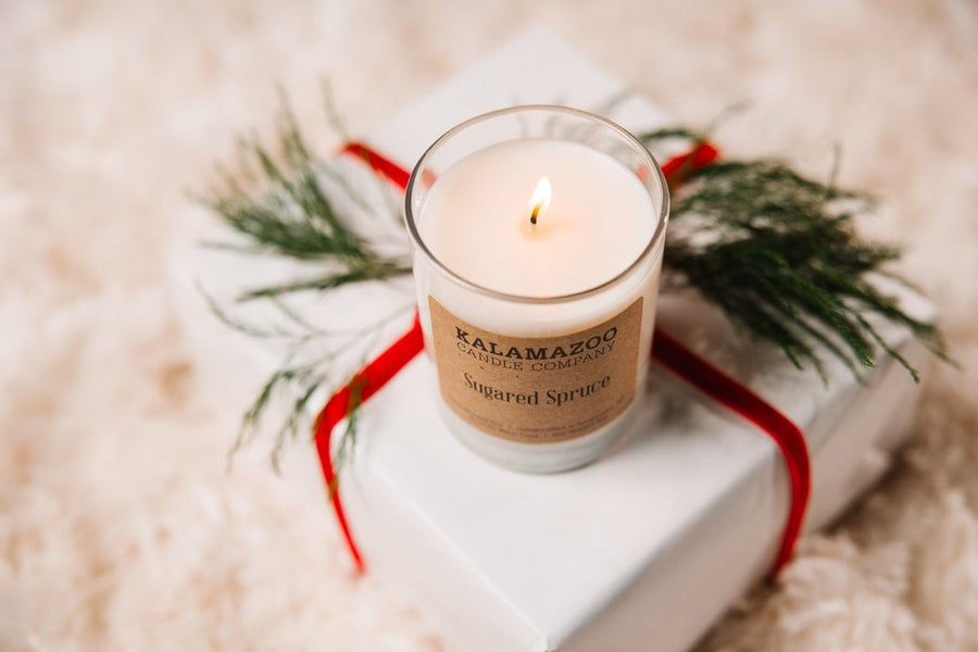Lit Sugared Spruce soy candle on a wrapped gift with a red ribbon and evergreen