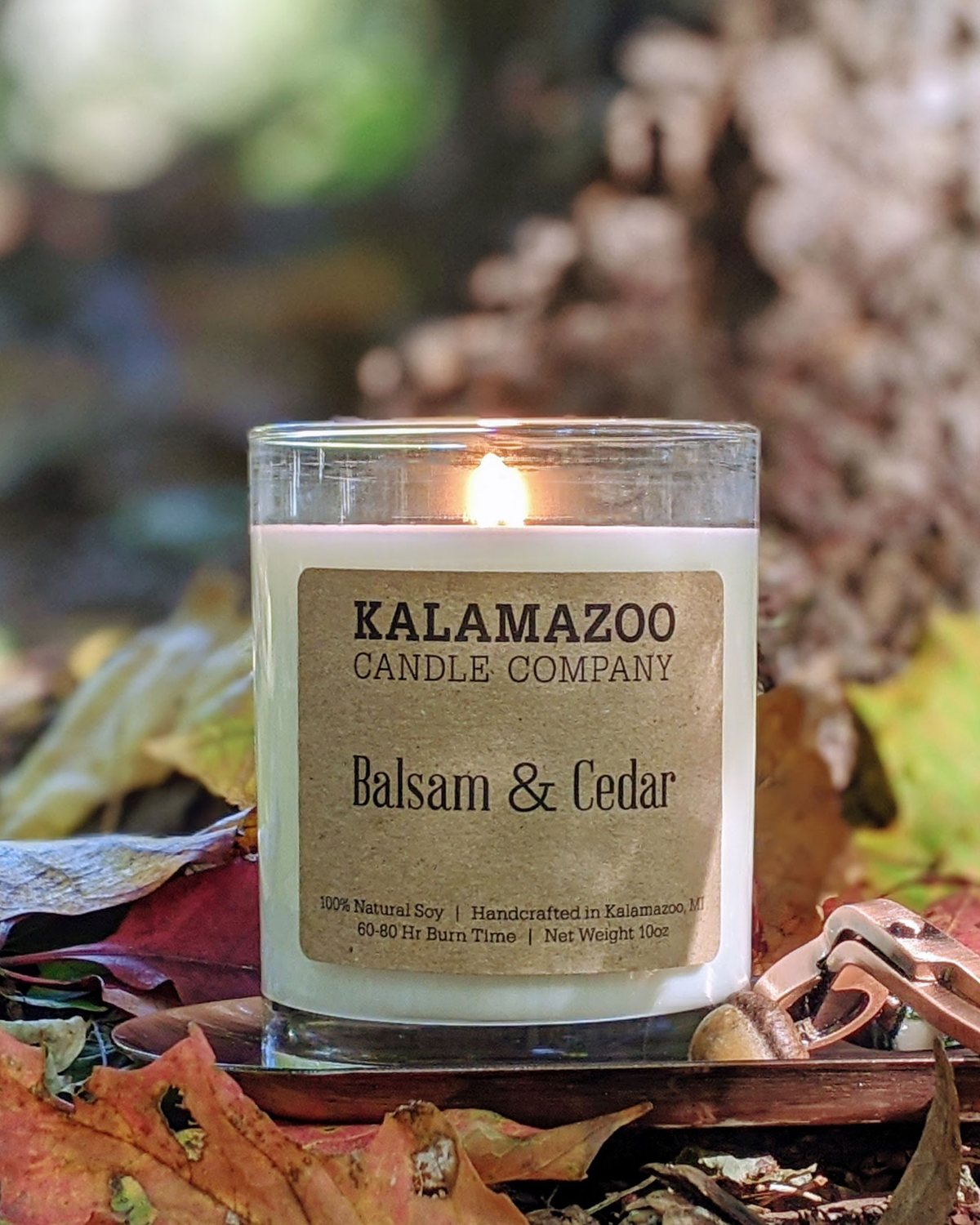 Lit Balsam & Cedar soy candle among colorful fall leaves