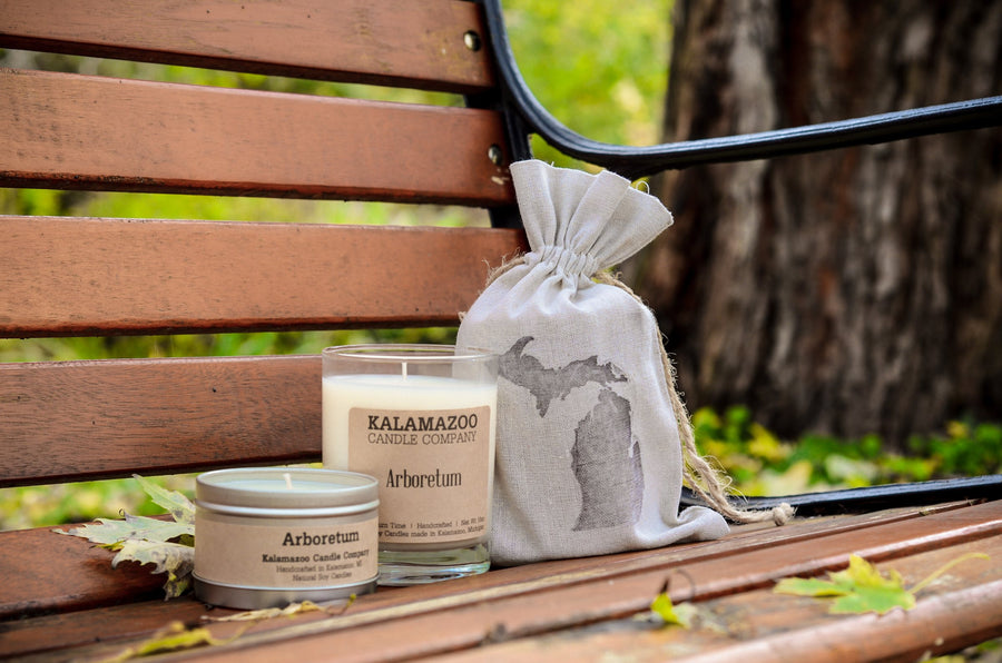 Arboretum soy candle jar and travel tin on a park bench with a Michigan gift bag