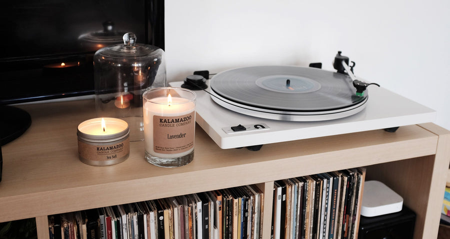 Lit Lavender soy candle and Sea Salt travel tin on a shelf next to a record player