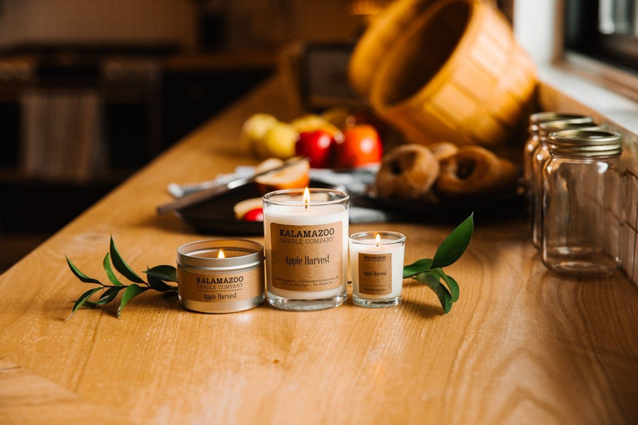 Apple Harvest soy candle jar, travel tin and votive lit on a kitchen counter with apples and cider donuts