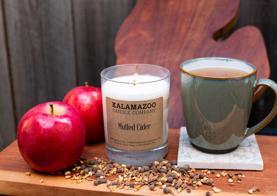 Lit Mulled Cider soy candle with red apples, a mug of cider and mulling spices