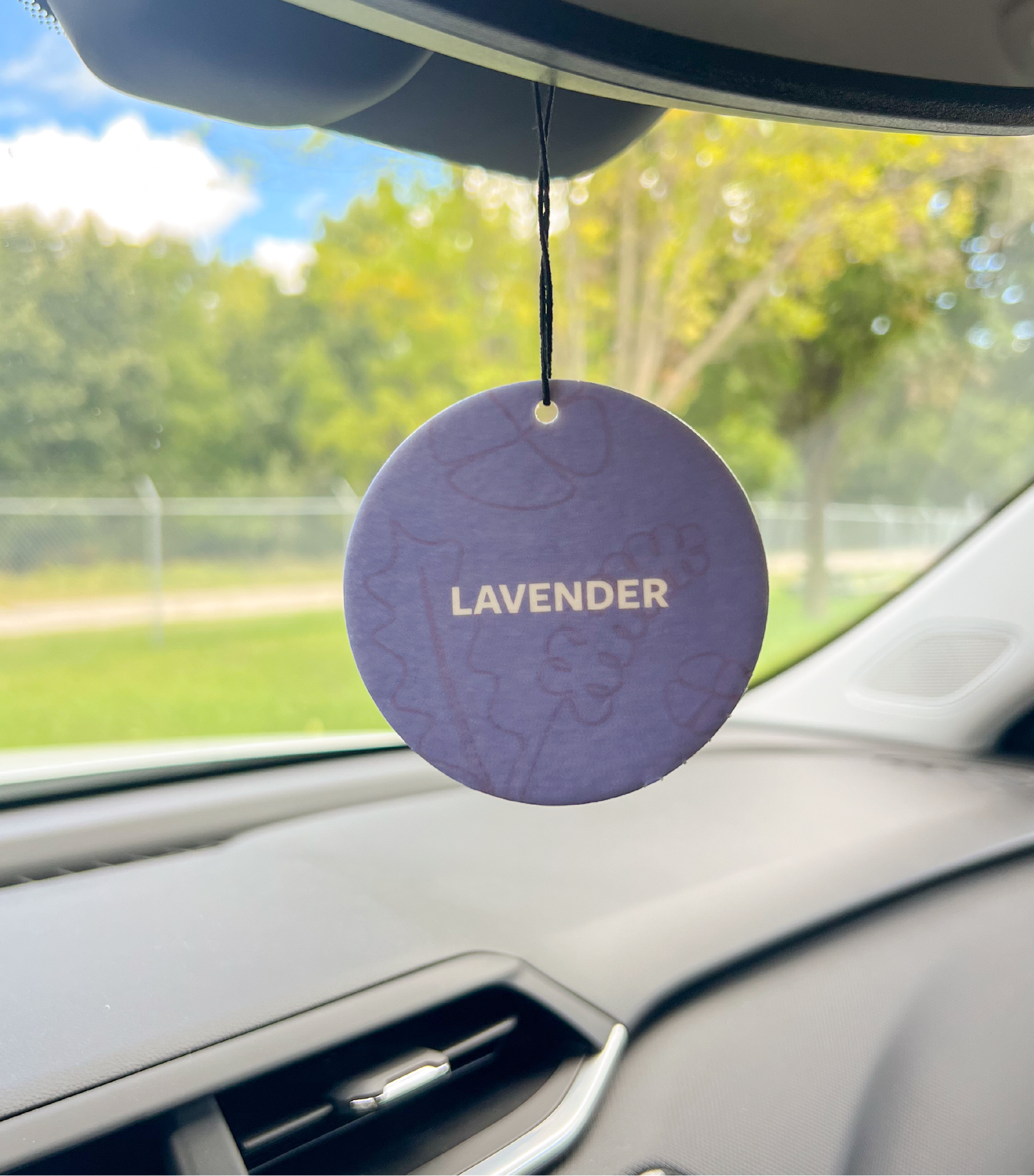 The front of a lavender car freshener hanging in a car.