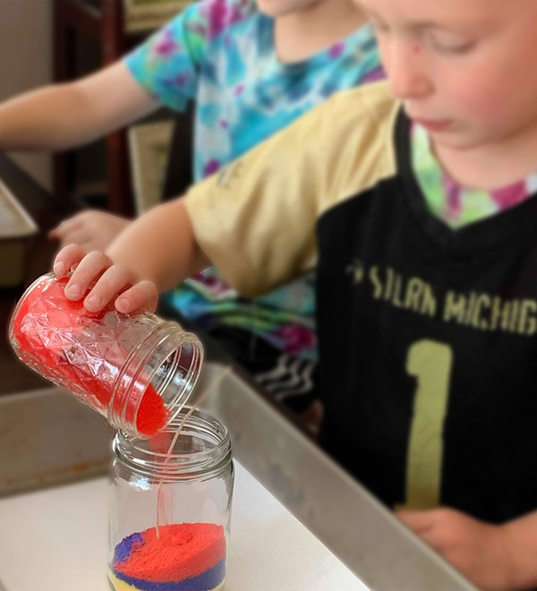 Child pouring colored sand to make a sand candle