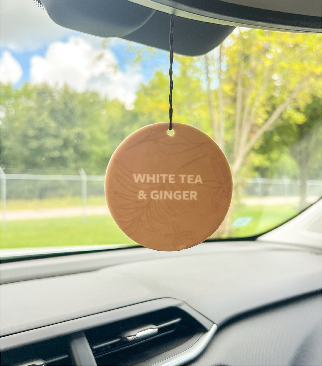 A White Tea & Ginger Car Freshener Hanging in a car.
