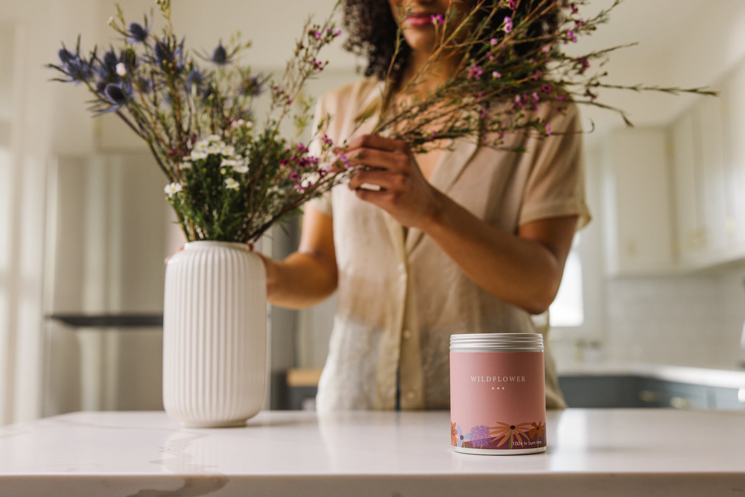 A Wildflower candle next to a vase of wildflowers