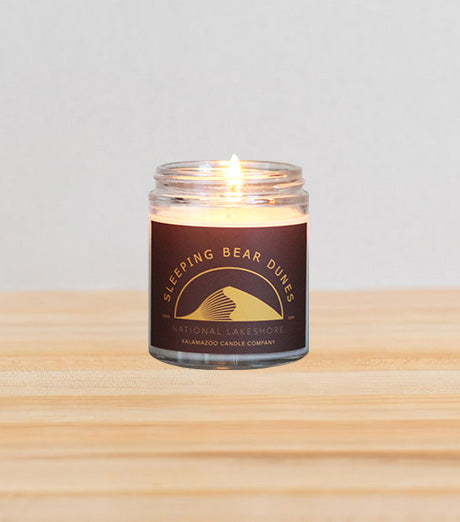 Graphic Sleeping Bear Dunes National Lakeshore jar candle filled with a warm and exotic earthy blend of sandalwood, bergamot, and nutmeg.